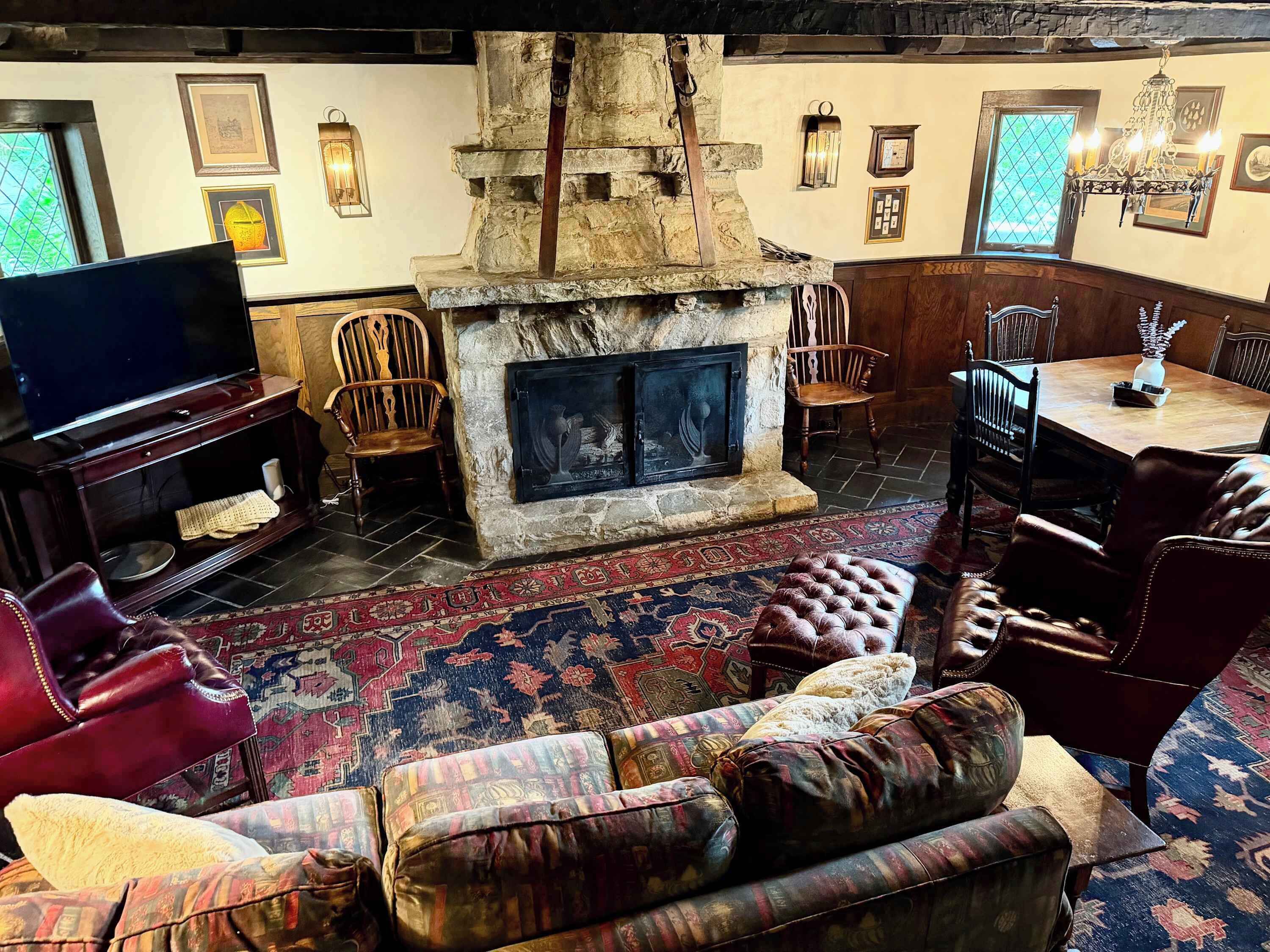 A traditional living room with a stone fireplace, a television, leather furniture, and a patterned rug.