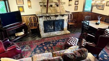 A traditional living room with a stone fireplace, a television, leather furniture, and a patterned rug.