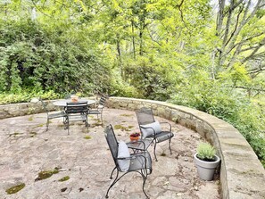 An outdoor patio with a stone table and metal chairs, surrounded by lush greenery and stone walls. - Tynecastle Retreat - Views, Game Room & Patio (Banner Elk)