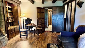 A room with a wooden floor, a chess table, a blue sofa, a patterned ottoman, and a bookshelf.