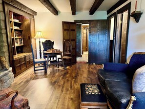 A room with a wooden floor, a chess table, a blue sofa, a patterned ottoman, and a bookshelf.