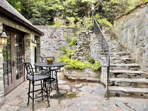 A stone staircase leading up to a stone wall, a table with chairs, and a potted plant.