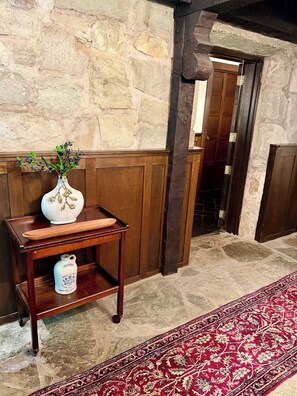 Un mur en pierre, des meubles en bois, un tapis rouge à motifs et une porte dans une pièce.