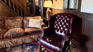 A traditional interior with a wooden staircase, a patterned sofa, a leather armchair, and a lamp.