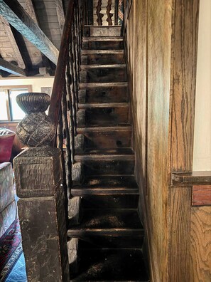 Una escalera de madera con barandilla que lleva a una habitación con un jarrón decorativo grande y una alfombra estampada.