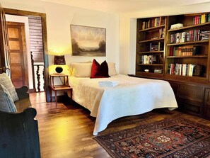 A bedroom with a bed, a bookshelf, a painting, and a wooden door.