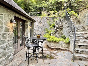 A stone building with a small outdoor seating area featuring a table and chairs, a lantern, and a staircase leading up.