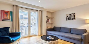 Ein modernes Wohnzimmer mit einer Couch, einem Sessel, einem Couchtisch und einem Balkon mit Blick auf Gebäude.