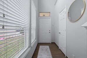 Un couloir avec une porte blanche, une petite fenêtre et un miroir accroché au mur.