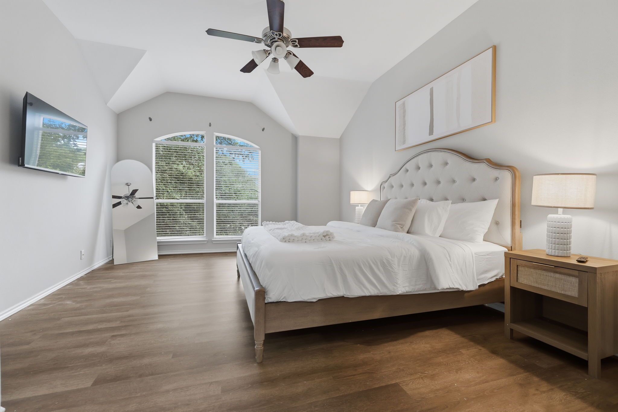 A bedroom with a bed, a nightstand, a ceiling fan, a window with blinds, and a door.