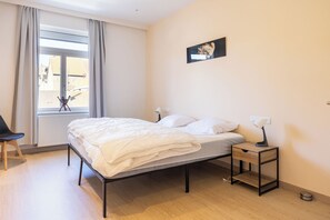 Une chambre à coucher avec un lit, une table de chevet, une lampe et une fenêtre avec des rideaux.