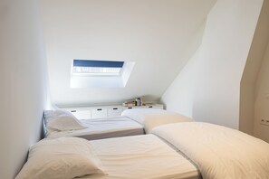 Ein Schlafzimmer mit zwei Betten, einem Oberlicht, einem Nachttisch mit Büchern und einer Steckdose.