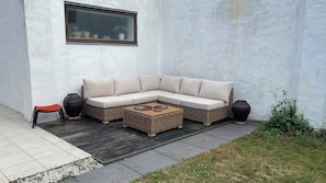 A sectional sofa with cushions, a small wooden table with coasters, a red stool, and two large vases against a white wall.