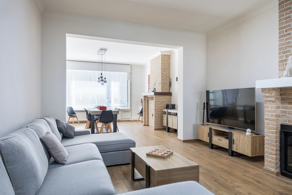 A modern living room with a grey sofa, a wooden coffee table, a TV, and a brick fireplace.