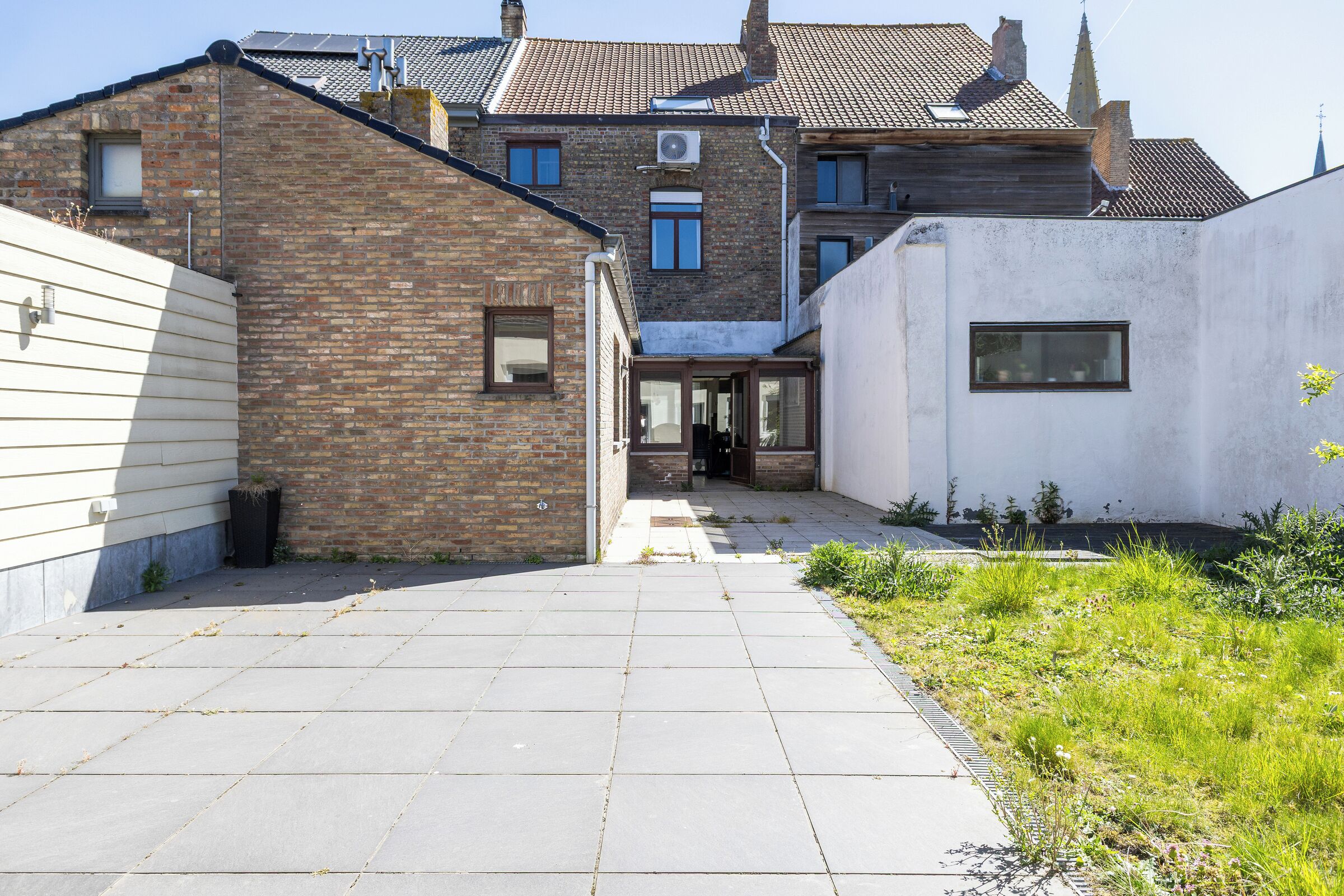 A courtyard with a paved walkway, a brick building, and a white building with a window.