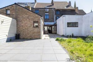 Une cour avec un chemin pavé, un bâtiment en briques et un bâtiment blanc doté d’une fenêtre.