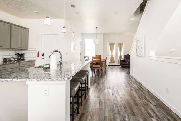 A modern kitchen with a marble countertop, bar stools, and a dining area with a wooden table and chairs.