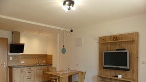Cozinha moderna com armários de madeira, fogão embutido e TV de tela plana fixada em uma parede de madeira.
