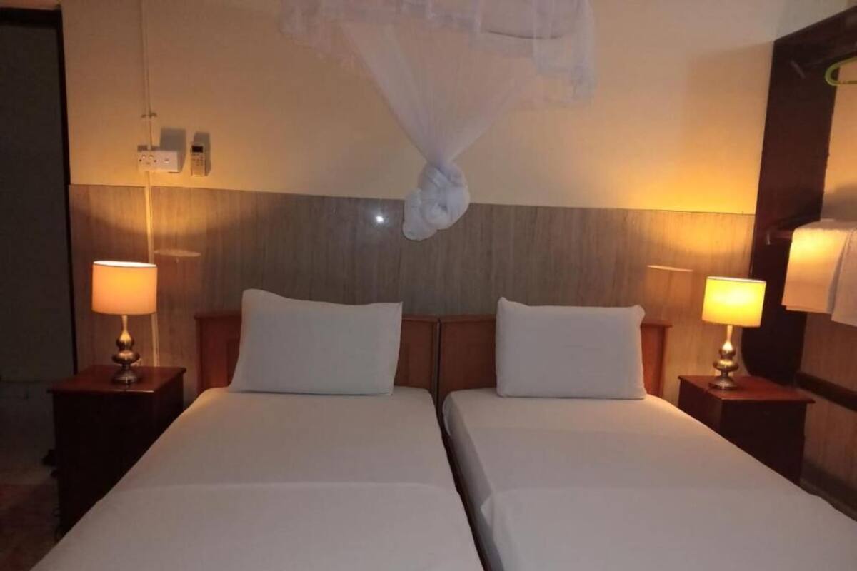 Hotellihuone, jossa on kaksi sänkyä, yöpöytävalaisimet, puinen pääty ja seinään kiinnitetty puhelin.