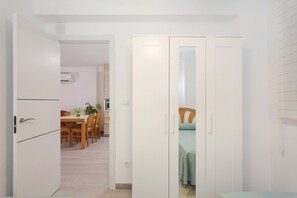 Un couloir mène à une salle à manger équipée d’une table et de chaises, ainsi qu’à un placard doté d’un miroir.