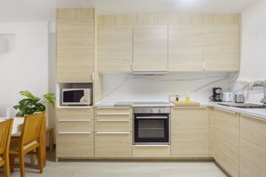 A modern kitchen with wooden cabinets, a microwave, an oven, and a dining area with chairs and a table. - ‘Luz y Playa’ Apartment with Private Terrace, Wi-Fi, and Air Conditioning (Cullera)