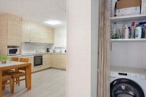 A modern kitchen with wooden cabinets, a microwave, an oven, and a dining table with chairs. - ‘Luz y Playa’ Apartment with Private Terrace, Wi-Fi, and Air Conditioning (Cullera)