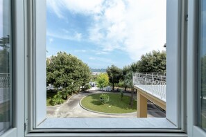 A view through a window of a courtyard with trees, a bridge, and a building in the background.