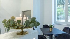 Een kamer met een witte tafel, een kleine plant in pot en een raam met uitzicht op groen.