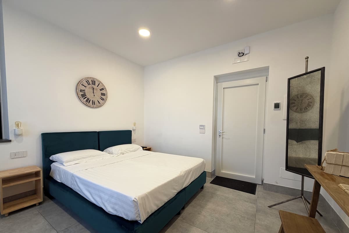 Een slaapkamer met een bed, een klok, een deur, een klein tafeltje en een bank.