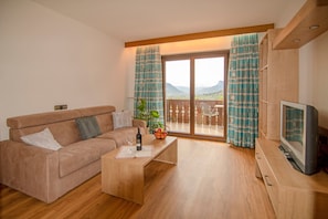 Ein Wohnzimmer mit Sofa, Couchtisch, Fernseher und einem Balkon mit Vorhängen.