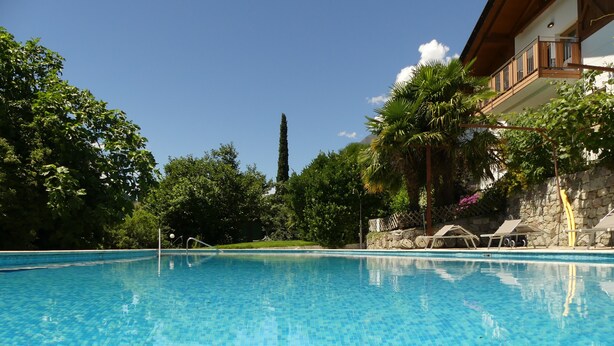 Una piscina blu cristallina con lettini da sole e un muro in pietra.