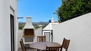 Un pati amb una taula i cadires de fusta rodona, una xemeneia, i vistes al paisatge.