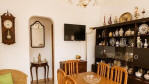 Un comedor con una mesa y sillas de madera, un candelabro, un televisor y una estantería con diversos objetos decorativos.