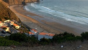 Paisaje costero con acantilados, una playa y un pequeño poblado con edificios y coches aparcados.