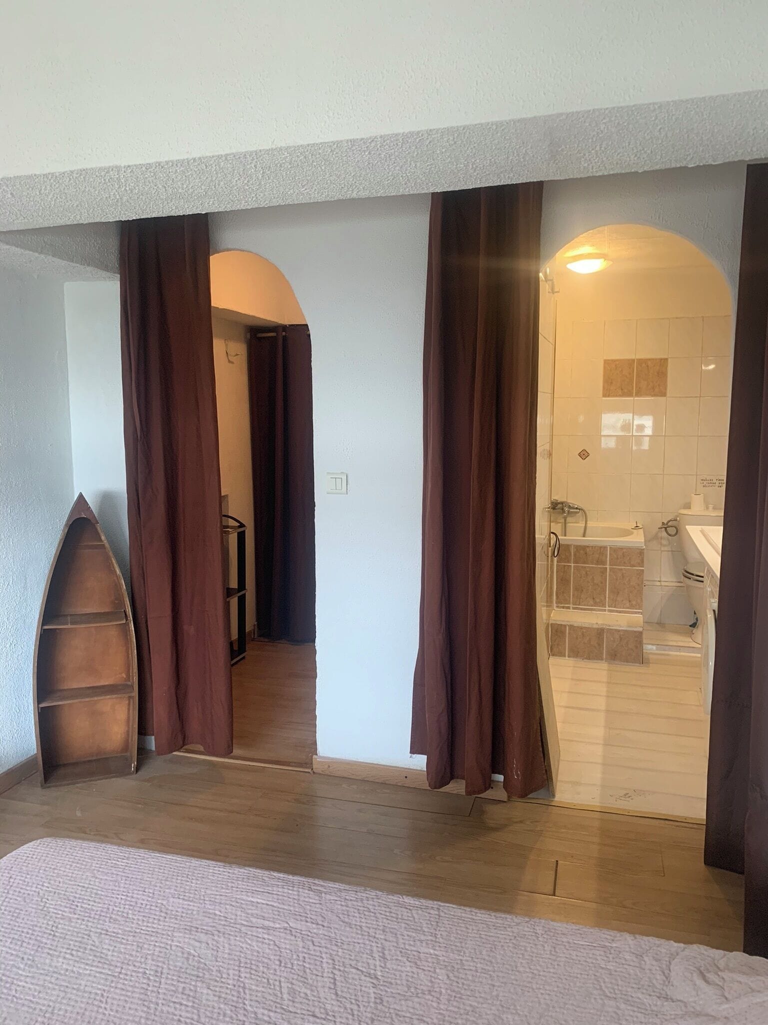 Ein Schlafzimmer mit einem Bett, einem Holzregal und einem Badezimmer mit Waschbecken und Toilette.