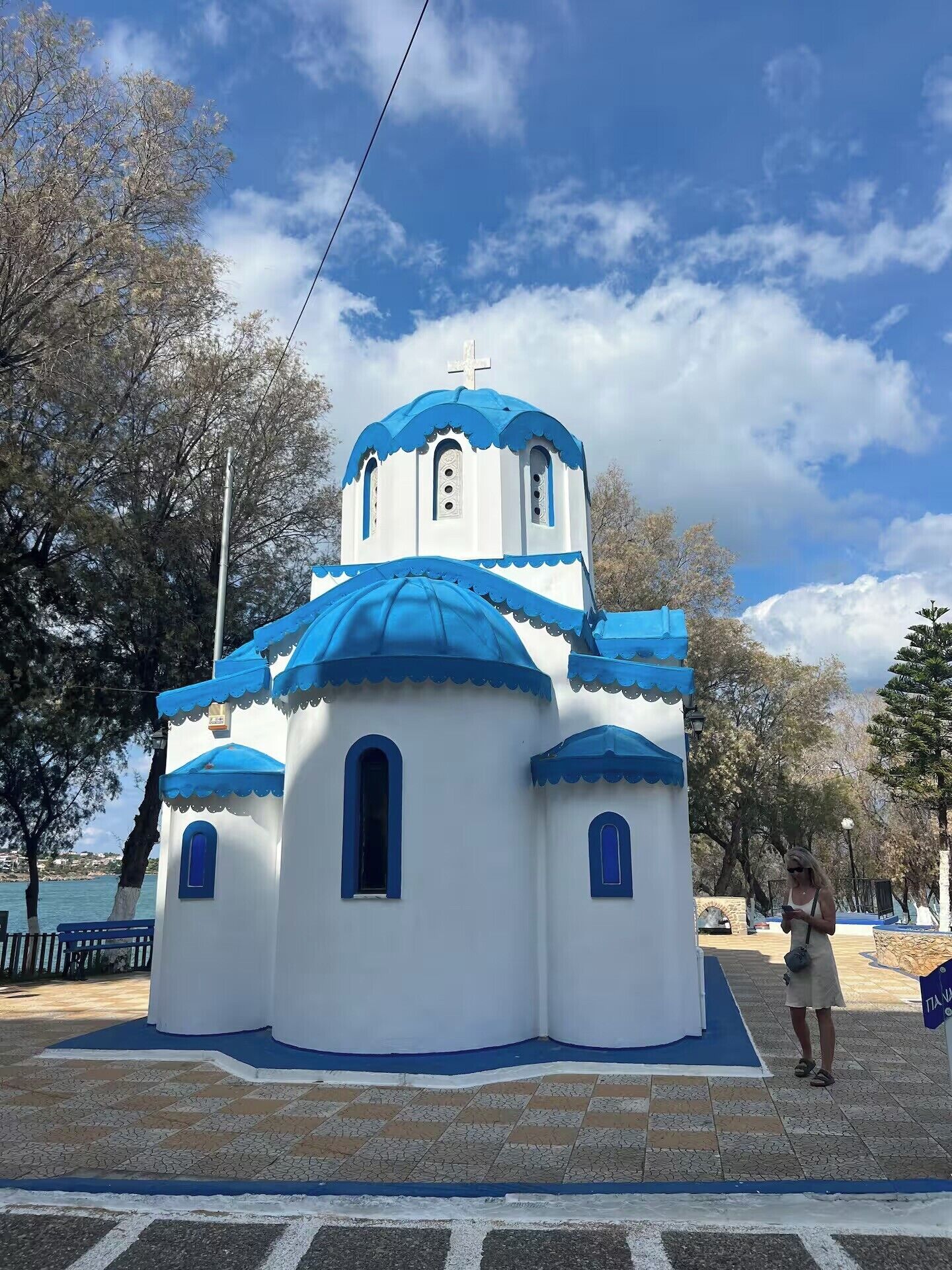 Une petite église blanche et bleue, surmontée d’une croix, entourée d’arbres et baignée par un ciel dégagé.