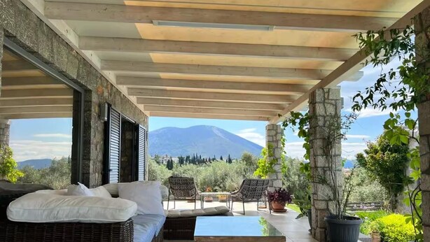 A covered patio with wicker furniture, a glass-top table, and potted plants. - Aegean Retreat for 6 Pool & Evia Views Near Athens (Chalcis)