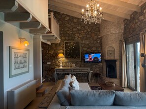 Una sala de estar con pared de piedra, una araña, un televisor, una chimenea y un sofá.