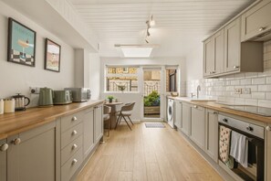 Een moderne keuken met houten aanrecht, een eethoek met stoelen en een uitzicht door een deur op een buitenruimte.