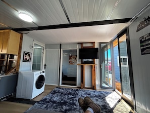 A laundry area with a washing machine, a rug, and a television on a wooden stand. - Tiny home available in Algona Pacific.  Right off of 167 close to amenities. (Pacific)