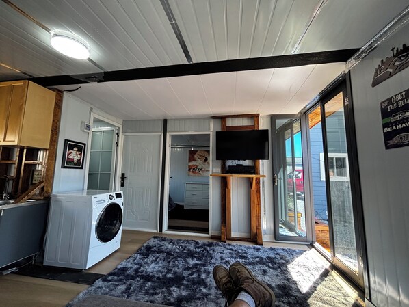 A laundry area with a washing machine, a rug, and a television on a wooden stand.