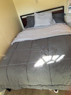 A bed with a grey quilt and striped pillow, a wooden headboard, and a nightstand with a water bottle. - Adorable private room at side of house  in Norwalk perfect for your next getaway (Norwalk)