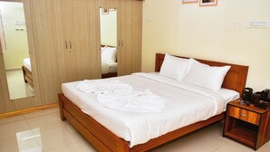 A neatly made bed with white linens, a wooden nightstand with a remote control, and a wardrobe with a mirror.