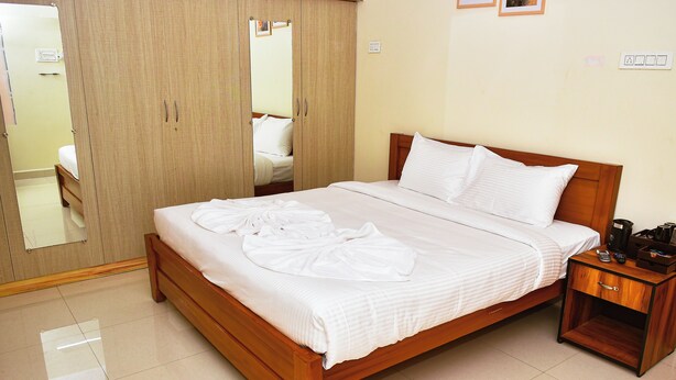A neatly made bed with white linens, a wooden nightstand with a remote control, and a wardrobe with a mirror.