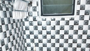 A bathroom with a checkered tile wall, a toilet, and a window.