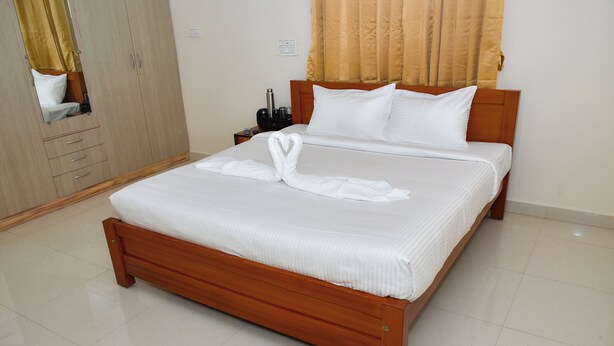A neatly made bed with a towel in the shape of a swan, a wooden headboard, and a nightstand with a bottle and a cup.