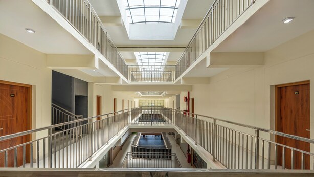 A multi-level hotel interior with a central atrium, metal railings, and a skylight.