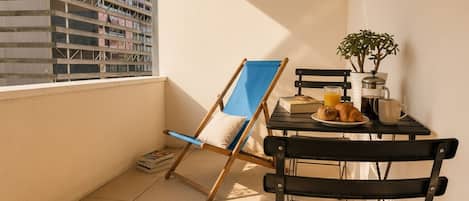 A balcony with a table, chairs, a plant, and a view of a building.