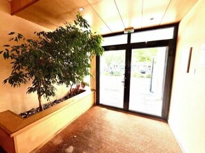 A reception area with a large potted tree, a reception desk, and a glass door leading outside. - Pleasant studio in La Rochelle (La Rochelle)