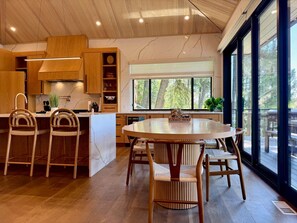 A modern kitchen with wooden cabinets, a central island, and a dining area with chairs.
